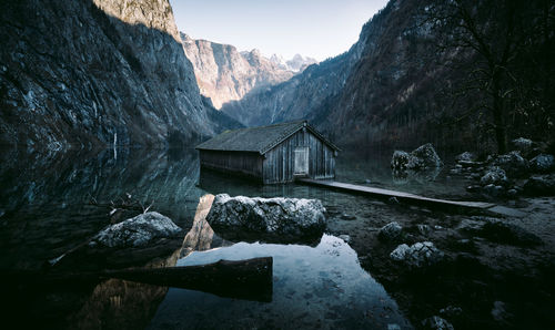 View of hut by lake against rock mountain