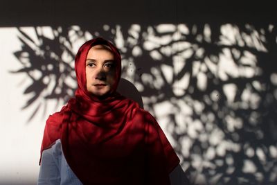 Portrait of young woman standing against red wall