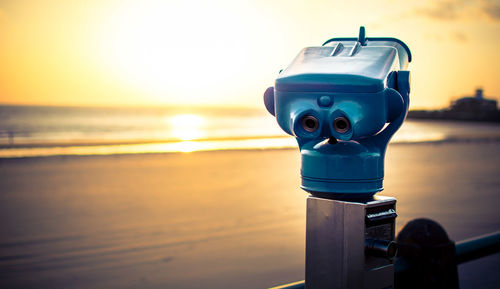 Close-up of coin-operated binoculars by sea against sky during sunset