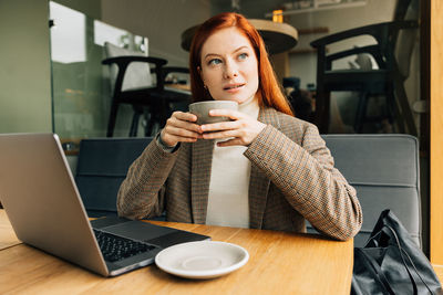 Young woman using laptop while sitting on table