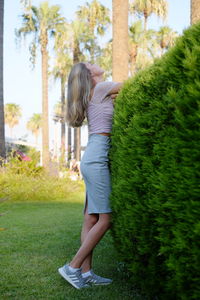 View of young woman standing at green hedge