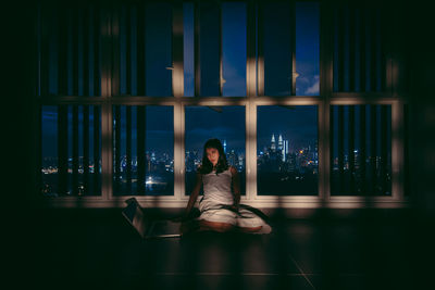 Woman sitting against glass window in darkroom