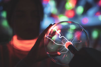 Close-up of woman wearing illuminated necklace holding lighting equipment in darkroom