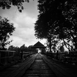 Empty footpath amidst trees in city against sky