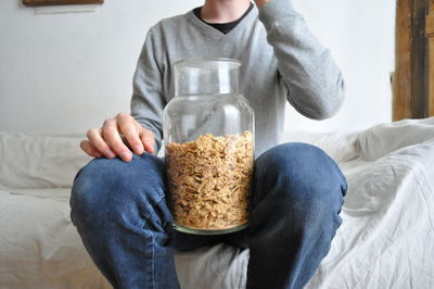 Midsection of man with food in jar sitting on bed