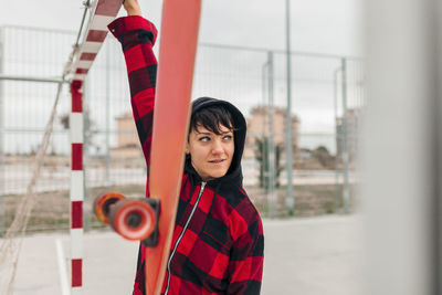 Portrait of young woman wearing hooded shirt leaning on sports goal