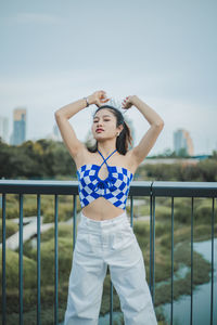 Portrait of young woman standing against railing