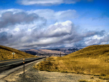 Road leading towards mountains against storm clouds