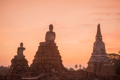 Low angle view of buddha statues and temple against sky during sunset