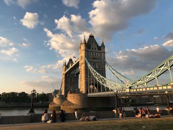 People at bridge over river against cloudy sky