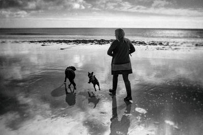 Rear view of friends walking on beach against sky