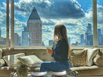 Woman sitting by modern office buildings against sky