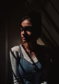 Young woman looking through window while standing against wall at home