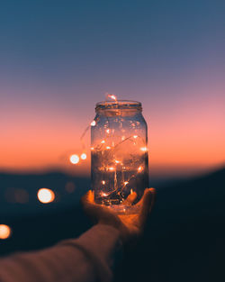 Close-up of hand holding illuminated light against sky at sunset