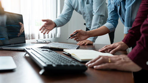 Midsection of colleagues discussing on desk in office