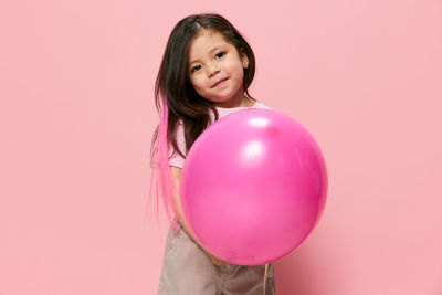 Portrait of young woman holding heart shape balloon against pink background