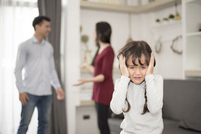 Close-up of girl crying while parents fighting in background at home