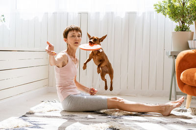 Cute woman is training her dog at home while sitting on floor. caucasian girl