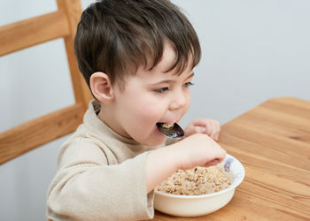 Little boy eating oatmeal for breakfast in the kitchen