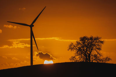 Silhouette of wind turbine against orange sky