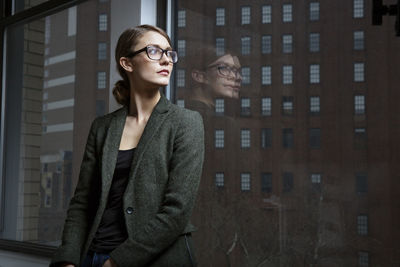 Businesswoman looking away while standing by window in office