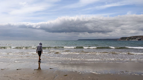 Rear view of man standing on beach against sky