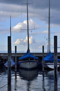 Boats in harbor against cloudy sky