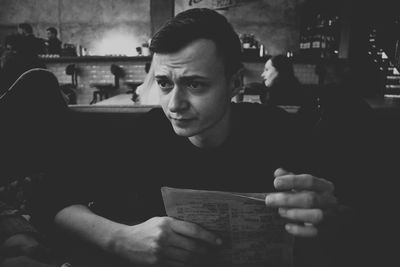 Young man with menu looking away while sitting in cafe