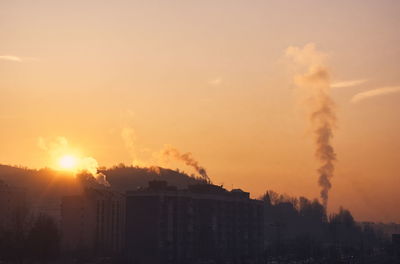 Smoke emitting from factory against sky during sunset