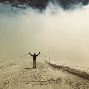 Rear view of man skiing on snow field against cloudy sky