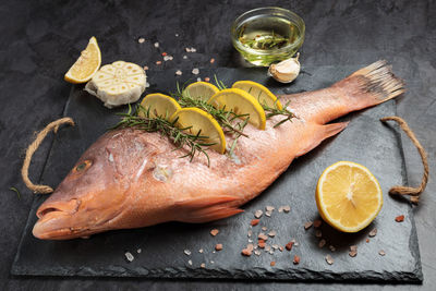 Freshly marinated raw red snapper fish with lemon slices, garlic and rosemary herbs, on dark