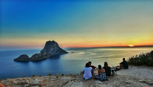 Friends sitting at beach against sky during sunset