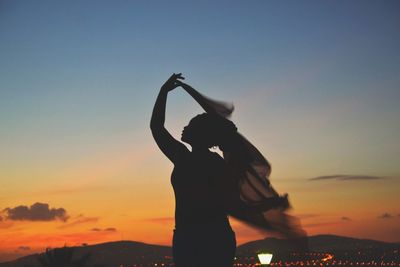Silhouette of woman holding scarf at sunset