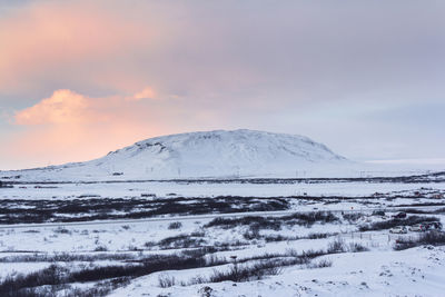 Snow covered landscape against sky during sunset