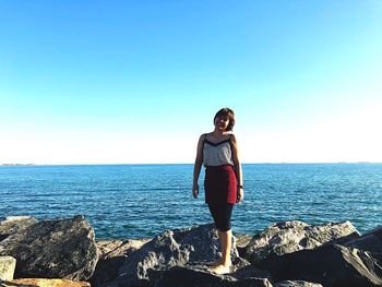 Man standing on rock by sea against clear sky