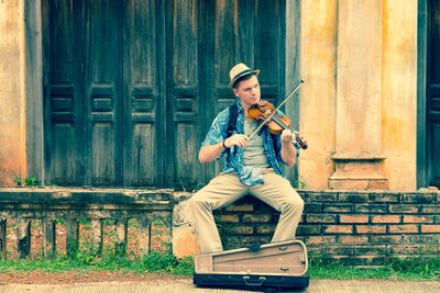 Man playing violin while sitting at window sill