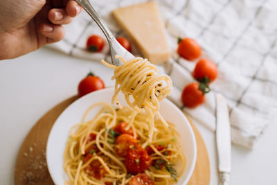 Spaghetti wrapped on a fork in the background of a portion of pasta with cherry tomatoes in a plate