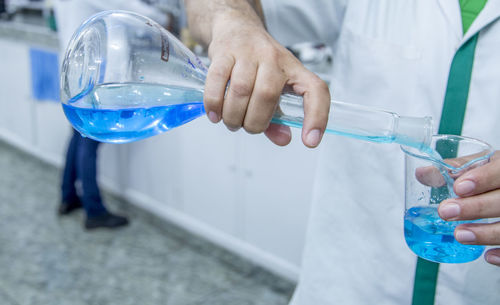 Midsection of scientist pouring liquid in beaker at laboratory