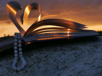 Bead necklace with heart shape folded pages of book during sunset