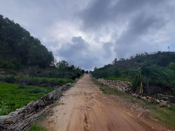 Dirt road amidst field against sky