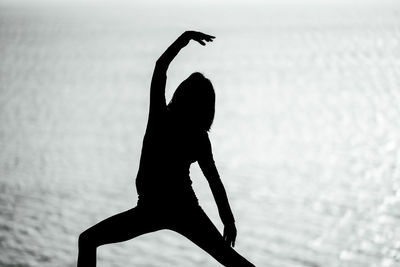 Low angle view of silhouette woman with arms raised standing on beach