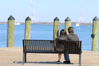 Rear view of friends sitting by sea against clear sky