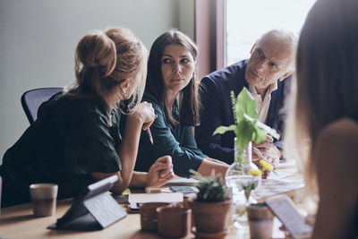 Female professionals planning strategy with businessman sitting at conference table during meeting in board room