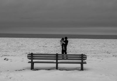 Father carrying daughter at beach against sky during winter