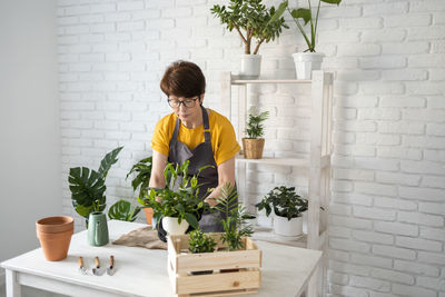 Side view of woman holding potted plant against wall