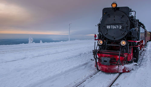 Train on snow covered field against sky during sunset