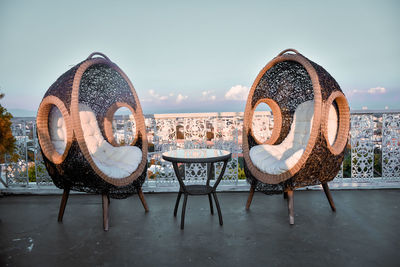 Empty chairs and tables at beach against sky