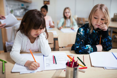 Students writing on paper at desk in classroom