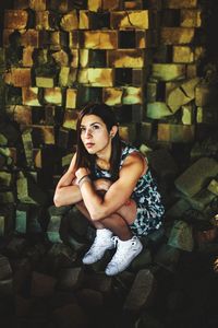 High angle view of thoughtful young woman crouching on broken paving stones