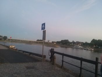 Road sign by river against sky in city